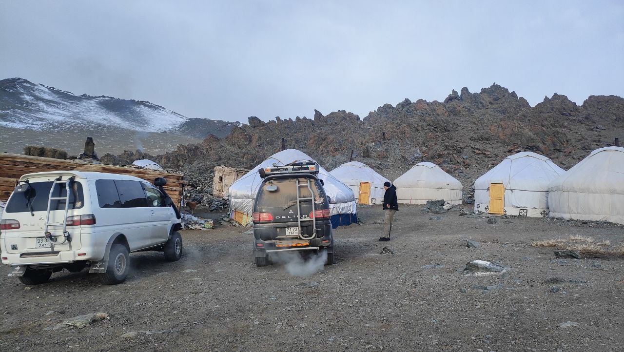 Mongolian gers and 4x4 vehicles at a remote Altai camp under snow-streaked mountains